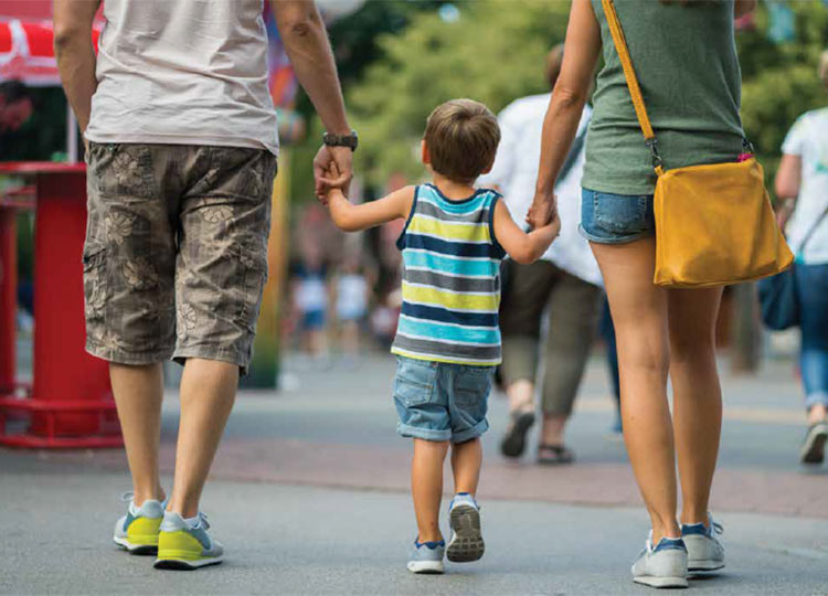 Photo of mother and father holding hands with child while walking.